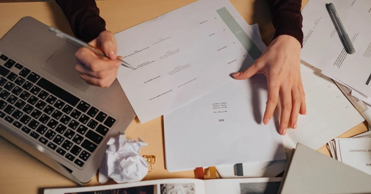 Hands sorting printed paper documents on a desk, the paper version of reordering PDF pages